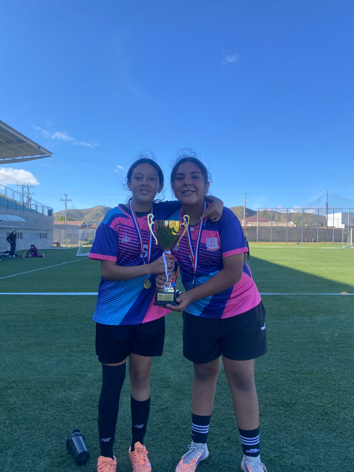 Dos jugadoras del equipo de fútbol femenino del CBO sonríen con la copa del tercer lugar y sus medallas